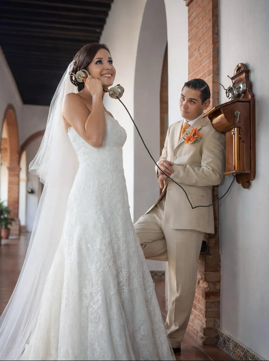 Bride speaking on a vintage wall telephone while the groom waits beside her, smiling