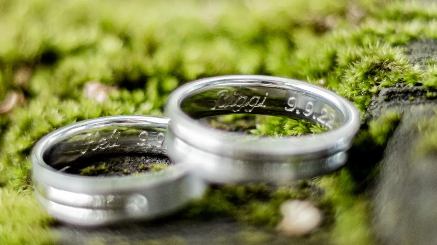 Engraved wedding rings resting on green moss, a detail from a wedding outdoors