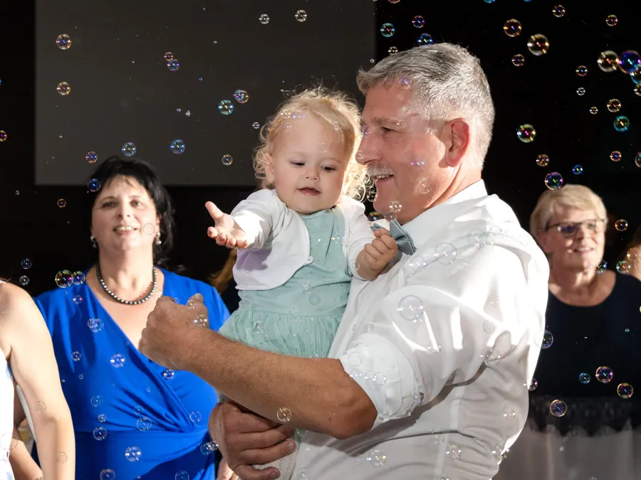 A grandfather dancing with his grandchild in a shower of bubbles, a joyful wedding party