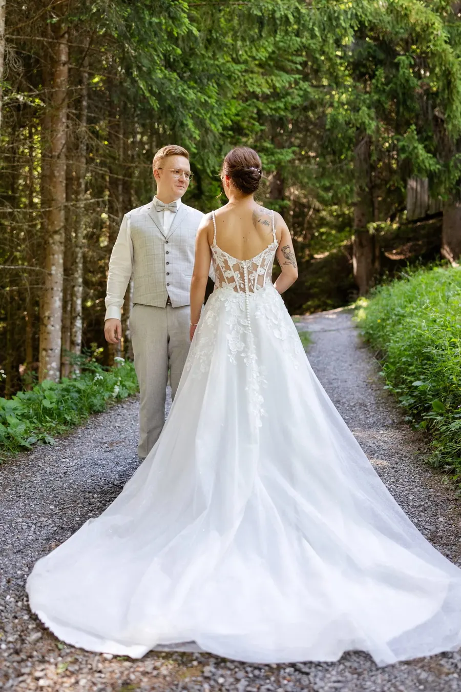 Bride and groom walking a forest path, the bride in a lace dress with a long train