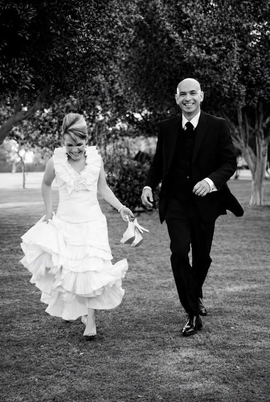 Laughing couple running barefoot across a meadow, black and white wedding reportage