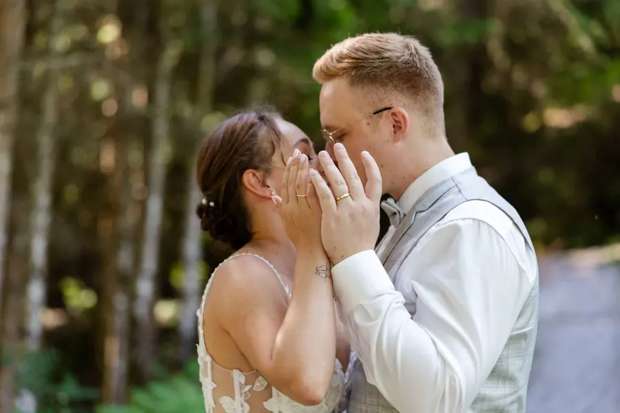 Couple kissing behind their hands, wedding rings in close-up, woodland wedding