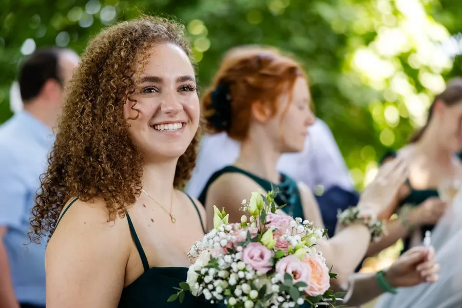 Bridesmaid holding the bouquet and smiling during drinks, summer wedding outdoors