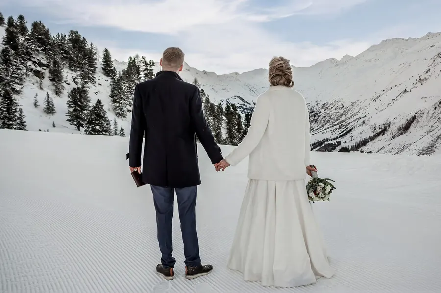Bride and groom hand in hand in the snow looking out over the Alps, winter wedding in Tyrol