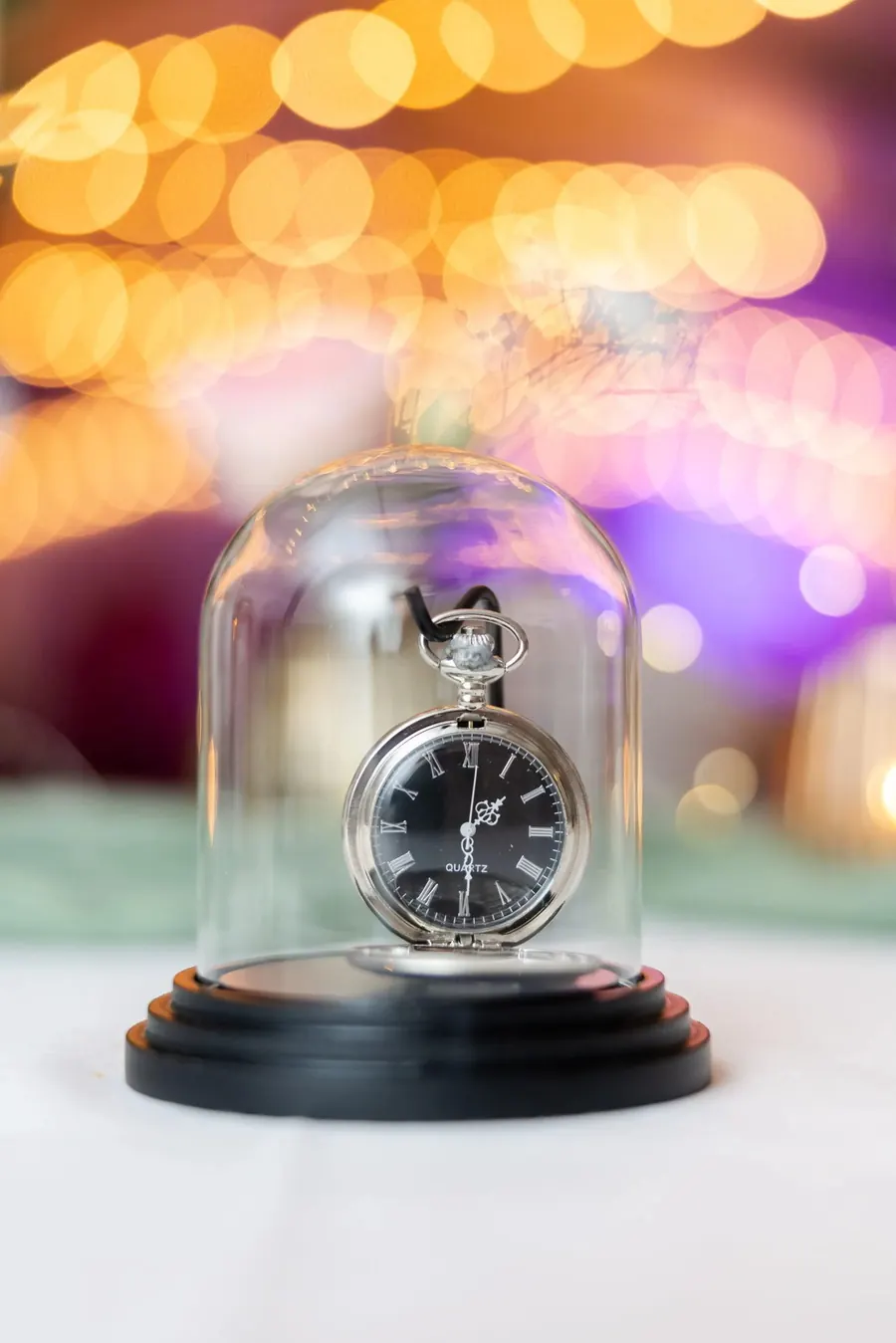 A pocket watch under a glass dome as wedding decor, lit by the lights of the party